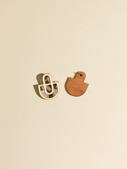 Two earrings, one gold and one wooden, on a beige background