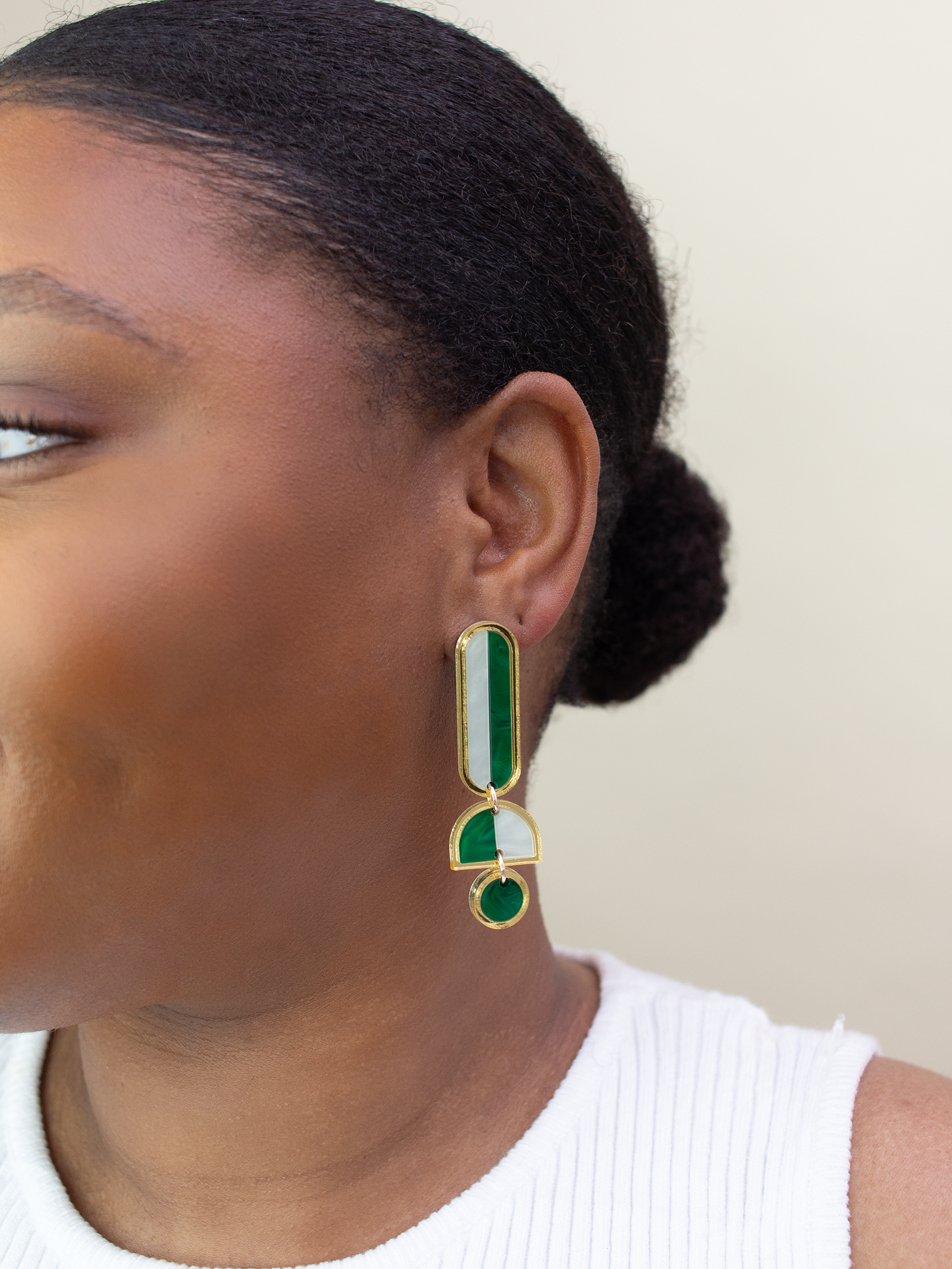 Close-up of a person wearing green and gold earrings against a neutral background