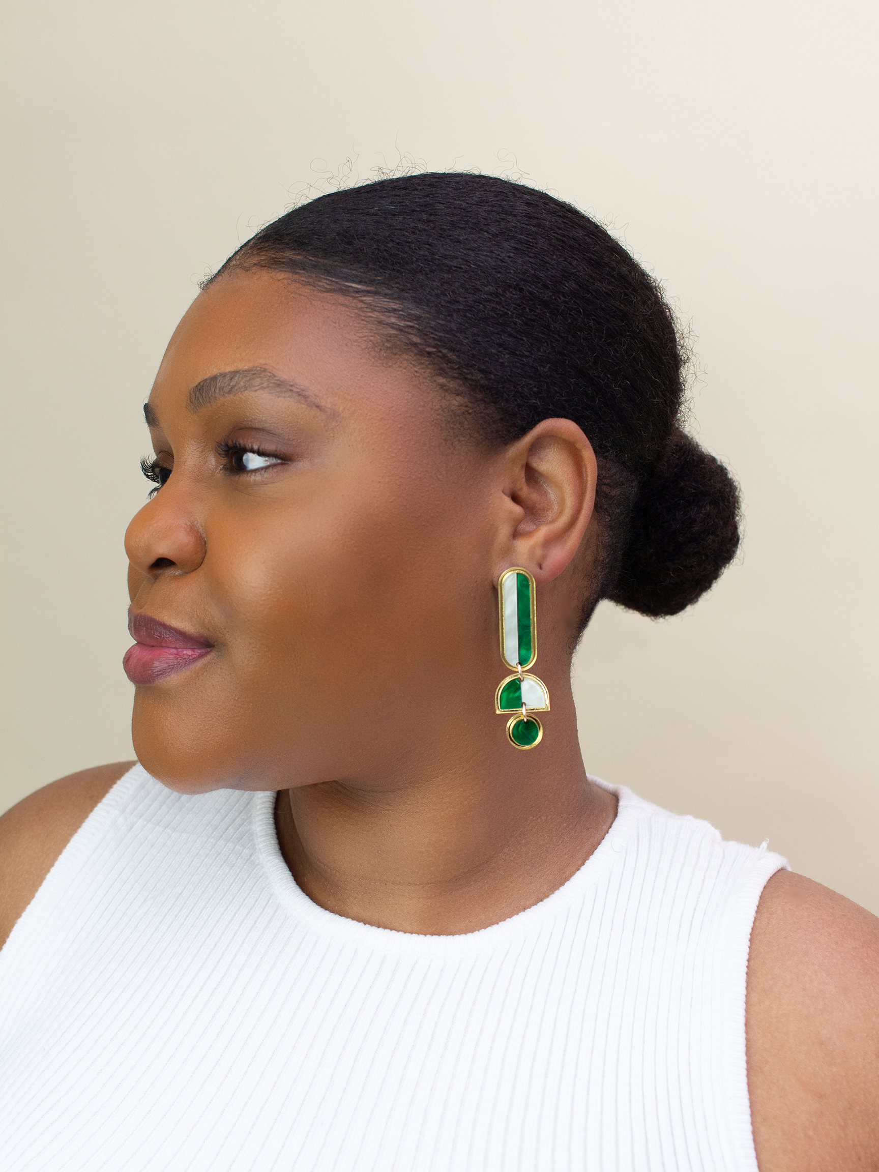 Woman wearing green and gold earrings against a neutral background