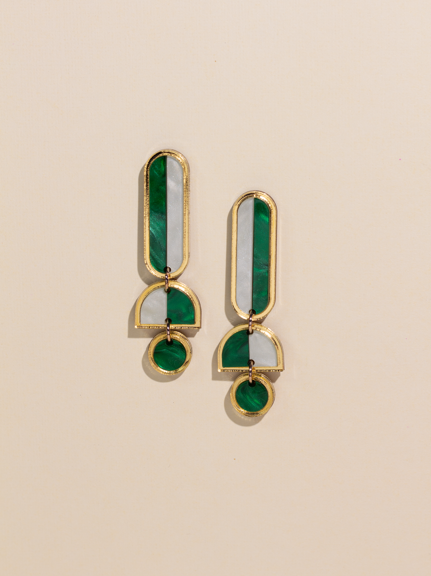 Pair of gold and green earrings on a beige background