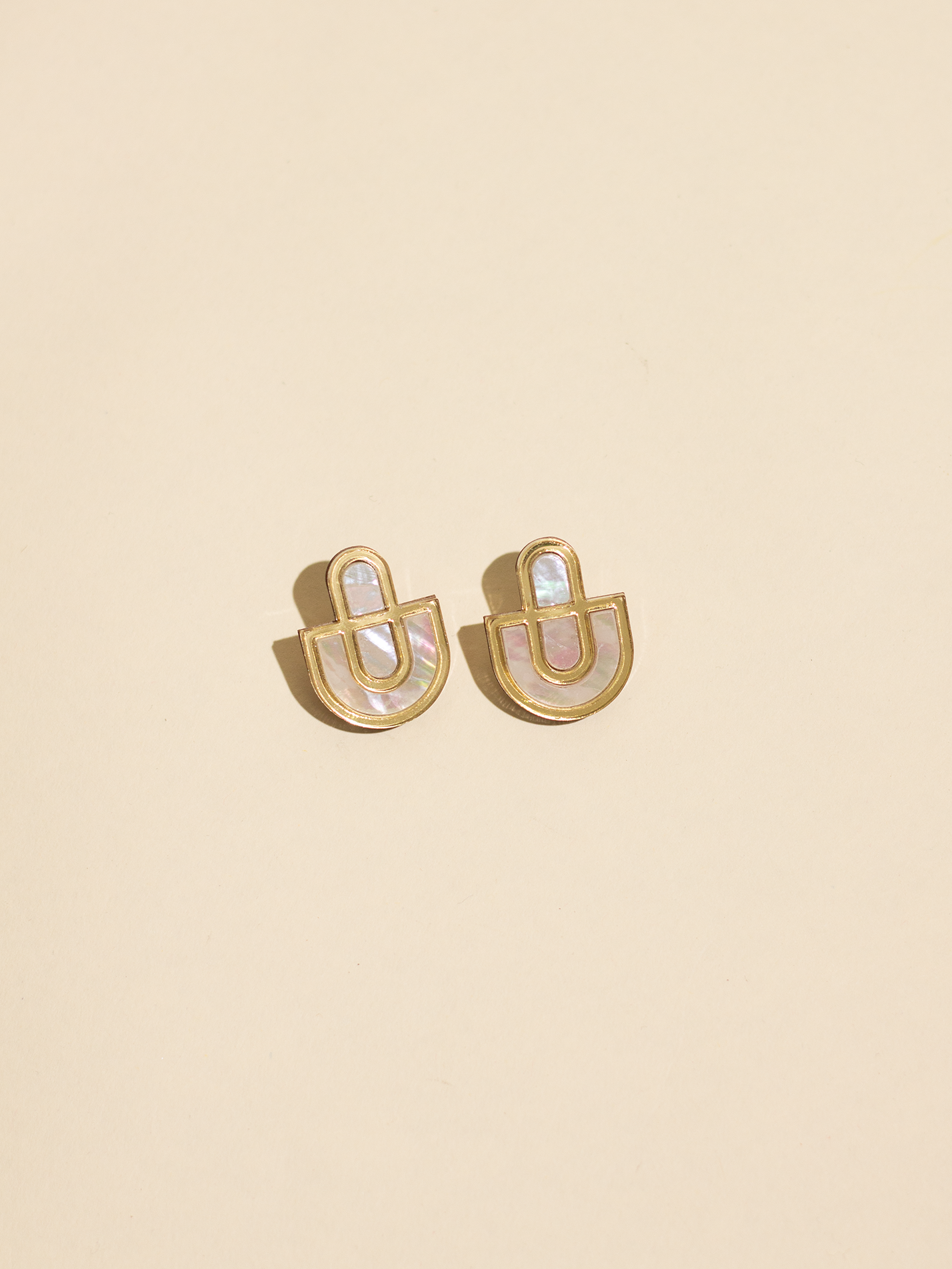 Gold earrings with a central gemstone on a beige background