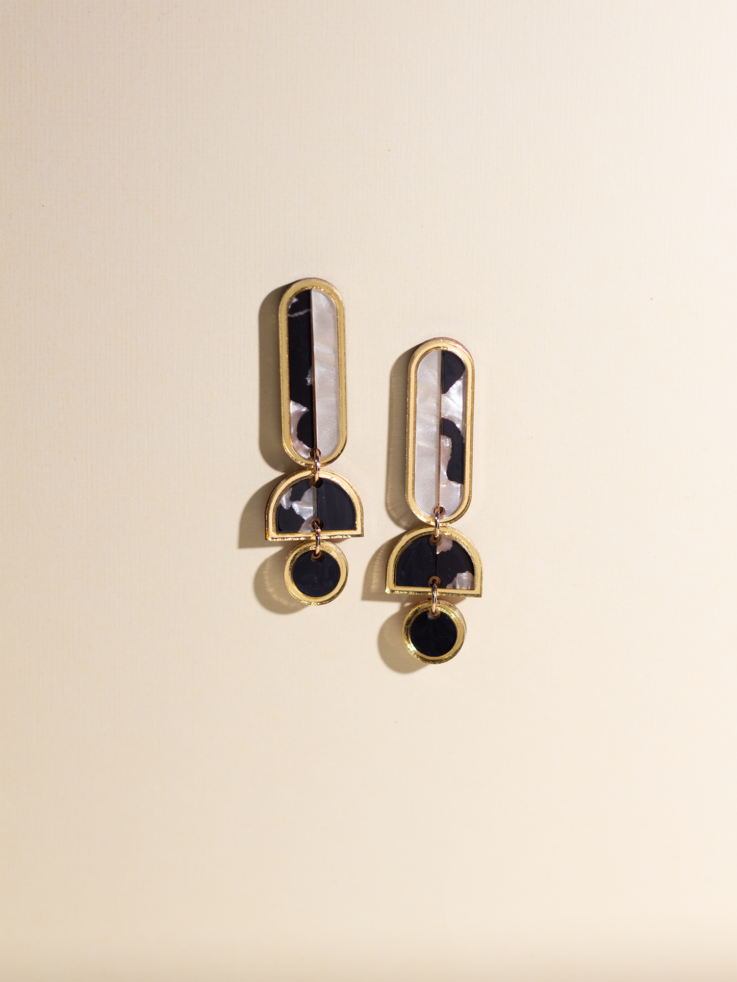 Pair of gold and black earrings on a beige background
